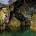 Lac souterrain. Un spéléo est accroché au mur au dessus de l'eau